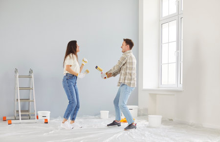 Married family couple dancing and having fun while painting walls during the renovation of new home. Family activity emphasizes joy and enthusiasm in creating a new living space together.の写真素材