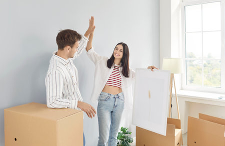 Happy married couple celebrating together by giving high fives while decorating or moving into new...