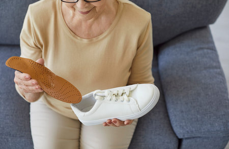 Top view of senior elderly woman wearing casual clothes sitting on sofa at home and inserting an orthopedic insole into a sneakers for comfortable footwear. Feet comfort and health concept.の写真素材