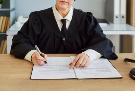 Female judge, wearing robe, writing document, handling legal process, in formal office, dealing with...