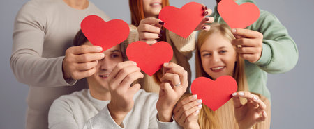 Several young people wishing you happy Valentines Day. Banner background with group of cheerful, joyful men and women smiling and holding beautiful red heart shaped paper cards in hands. Love conceptの写真素材