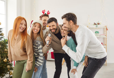 Friends celebrate New Year or Christmas with a lively karaoke party at home. Singing and music create a joyful atmosphere, marking the holiday with laughter and shared moments of celebration.の写真素材