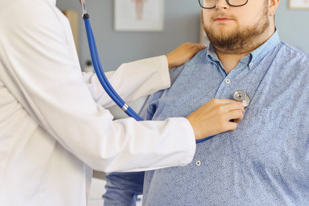 Doctor uses stethoscope for patient cardiology checkup. In the clinic, a physician conducts an examination of patient with obesity, heart and lungs. Theme: preventive healthcare and wellness.の写真素材