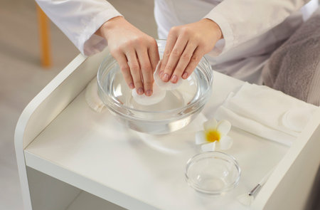 Closeup of female cosmetologist putting sponges into a bowl of water preparing for treatment procedure in spa salon. Professional beautician working in beauty salon. Wellness and skin care concept.の写真素材