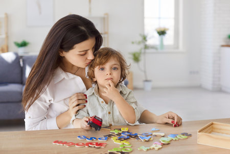Mother and son playing game with English alphabet letters. Mom and boy sitting together at table...