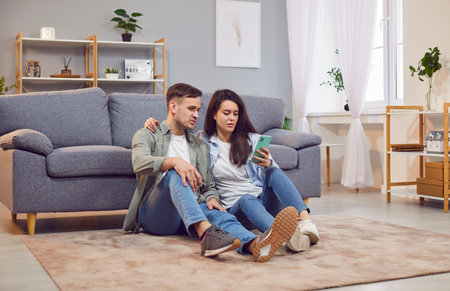 Family couple enjoying leisure time together at home, using a phone while sitting on the floor in...