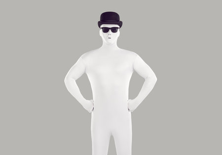 Portrait of faceless unrecognizable person wearing black hat and glasses in white spandex costume. Incognito man in bodysuit lokking confidently at the camera in studio isolated on grey background.の写真素材