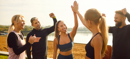 Happy smiling sporty group of people jumping standing in a circle in nature with hands up rejoicing the success in sport training or exercise achievement outdoors after workout in the park.の写真素材