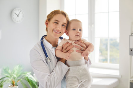 Portrait of a happy female doctor pediatrician or nurse holding a baby in a hospital clinic. Dedicated healthcare, patient support, and Medicare in a nurturing medical environment.の写真素材