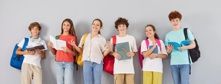 Diverse group of happy students stands together in a team portrait on a grey background, holding...