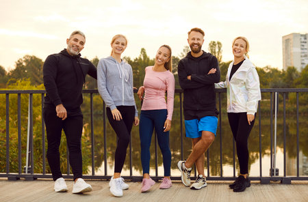 Portrait of a group of young athletic people on a city bridge. Happy smiling friends after training....