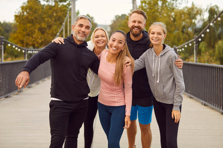 Portrait of a happy sporty people friends wearing sportswear hugging and looking cheerful at camera after successful workout in the park. Outdoors training and fitness in nature concept.の写真素材