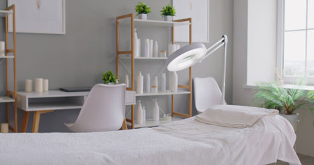 Cosmetology spa treatment room with a neatly made massage table, magnifying lamp, dermatology room. Professional massage setup for relaxing wellness treatments.の写真素材