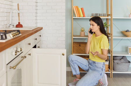 Woman calling in plumbing service as has problem with sink, using plunger, busy with housekeeping and household work, posing at kitchen, trying to dissolve blockage or to unclog drainの写真素材