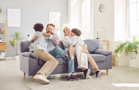 Young parents having fun with their children, hugging each other and playing together on sofa. Happy...