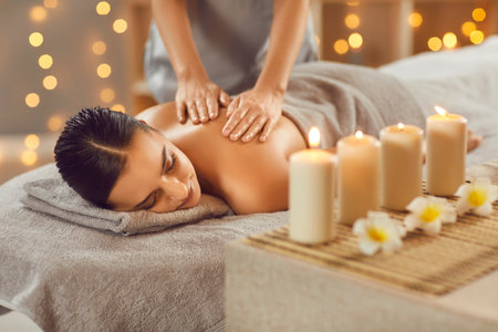Young woman relaxing in spa salon with hot stones along spine. Beautiful relaxed girl lying on couch enjoying hot stone massage in wellness center. Beauty treatment therapy, body care conceptの写真素材