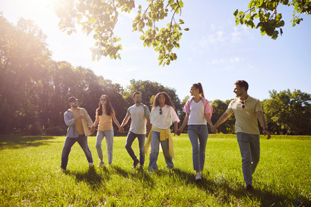Happy diverse group of friends, young people walking side by side across grassy field, green park,...