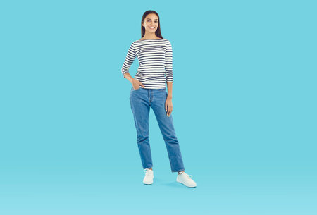Full body shot of a young woman wearing a comfortable striped three quarter sleeve top and blue...