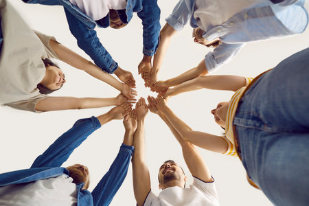 Happy team of young people raise their hands and join them together showing unity and solidarity....