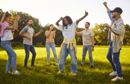 Group of a young diverse students having fun in summer park. Happy girls and boys dancing on green...