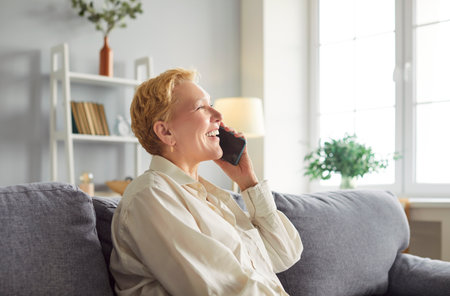 Portrait of senior mature smiling woman pensioner in casual clothes sitting on sofa in living room...