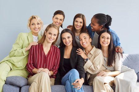 Happy smiling multiracial women team sitting on sofa, looking at camera and making group photo....