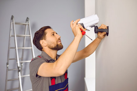 Service worker installing a modern security camera inside the house or apartment. Young man in a...