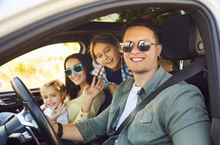 Happy family in car on road trip. Parents and children ride with safety, enjoying travel, sunlight,...