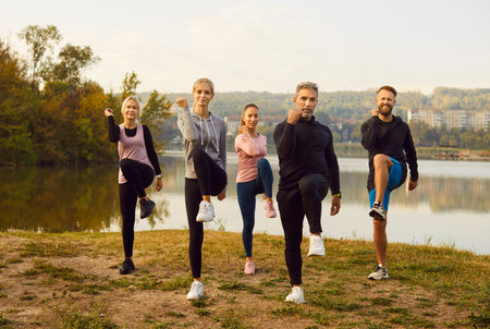 Happy smiling sporty group of people jumping standing in a circle in nature with hands up rejoicing the success in sport training or exercise achievement outdoors after workout in the park.の写真素材