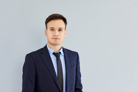 Close-up portrait shot of confident man in business suit isolated on light gray studio background with copy space. Professionak male entrepreneur looking at camera with serious facial expression.の写真素材