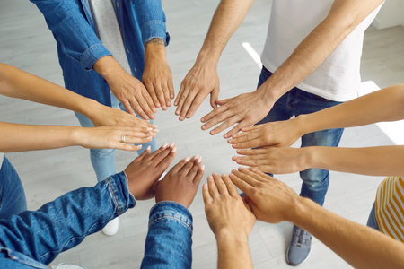 Team of friends joining hands. Group of different mixed race people in jeans and T shirts putting hands together. Cropped closeup shot, high angle. Teamwork, community, success, friendship conceptの写真素材