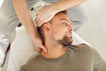 Close-up photo of adult Caucasian male patient in manual therapy office during osteopathic session. Professional male chiropractor specialist working with young man helping to cure neck pain.の写真素材