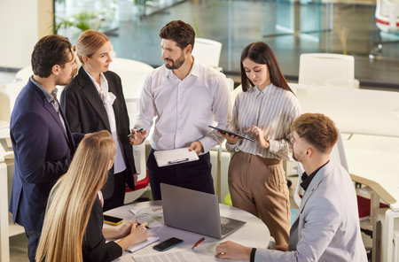 Group of business people working with financial documents during a meeting. Company employees talking in office making great decisions with brainstorming. Coworkers listen to colleague at workplace.の写真素材