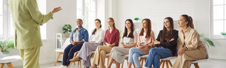 Cropped shot of coach telling something to happy multiracial female team sitting on chairs. Group of smiling women colleagues listening carefully during corporate training session in office. Banner.の写真素材