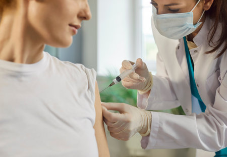 Close up of female patient receiving vaccine sitting in medical clinic. Doctor in mask and uniform giving injection in the woman shoulder in hospital. Vaccination and medicine concept.の写真素材