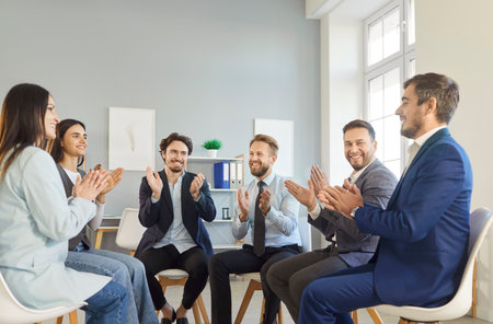 Smiling business team sitting in circle during office meeting and clapping hands together. Cheerful...