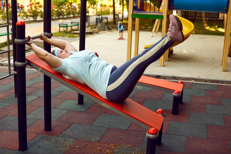 Strong adult woman in sportswear doing physical exercises on incline bench training equipment during...