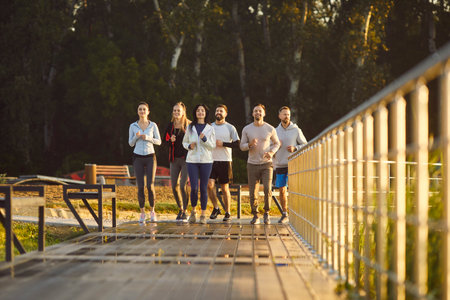 Group of people runs together outdoors during team workout, boosting running effort, uniting in...