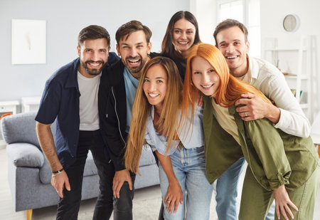 Group portrait of happy millennial friends, students or colleagues standing together in room and hugging each other. Six positive people man and women looking at camera and smiling. Friendship conceptの写真素材