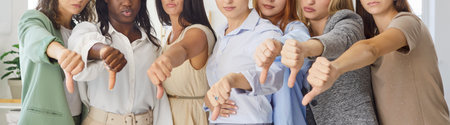 Women diverse group show thumbsdown gesture, express disapproval. A diverse female team indoors signals protest. Emotion shows rejection and unified dislike. Clear concept united female disapproval.の写真素材