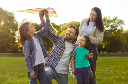Happy young family spending quality time together outdoors and flying colorful kite in park. Smiling parents and children enjoying leisure activity and bonding during sunny weekend on fresh air.の写真素材