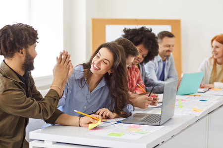 Happy young colleagues man and woman giving high five at meeting working together at desk with...