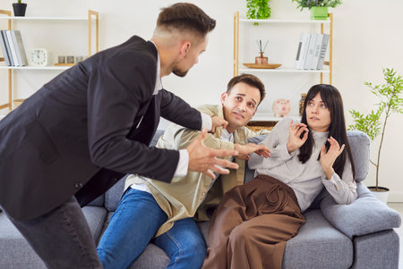 Emotional scene of love triangle at home where furious man argues with scared couple on sofa....