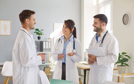 Medical staff of cheerful smiling young doctors standing on workplace in clinic discussing or planning treatment during a meeting in hospital. Healthcare, medicine and teamwork concept.の写真素材