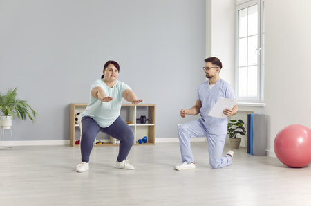 Doctor physiotherapist assists a plus-size patient during a rehabilitation session. Squats as part...