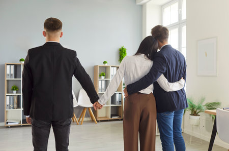 Back view in a modern office: the woman embraces her partner while holding another man's hand. A secret gesture exposes a complex situation.の写真素材