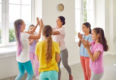 Female friendly choreographer giving high five to her happy smiling kids students girls in...