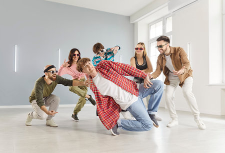 Group of young funny hipsters girls and guys dressed in modern clothes, wearing sunglasses, dancing together in modern dance school studio, spacious room. Youth culture, style and hobby conceptの写真素材