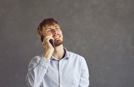 Studio headshot portrait of positive smiling caucasian man talking using mobile phone standing over...