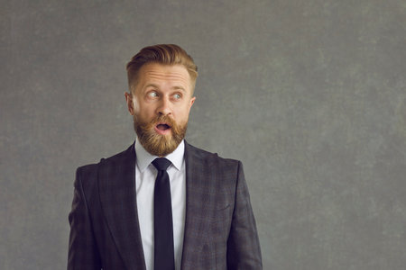 Studio headshot portrait of amazed adult caucasian businessman in formal suit and tie with opened mouth looking aside to copy space. Mature entrepreneur with surprised facial expressionの写真素材